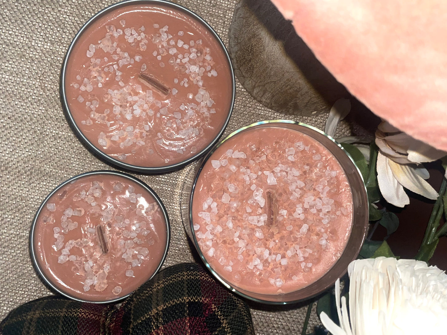 Three small round candles with a decorative top on a textured wax surface with flowers.