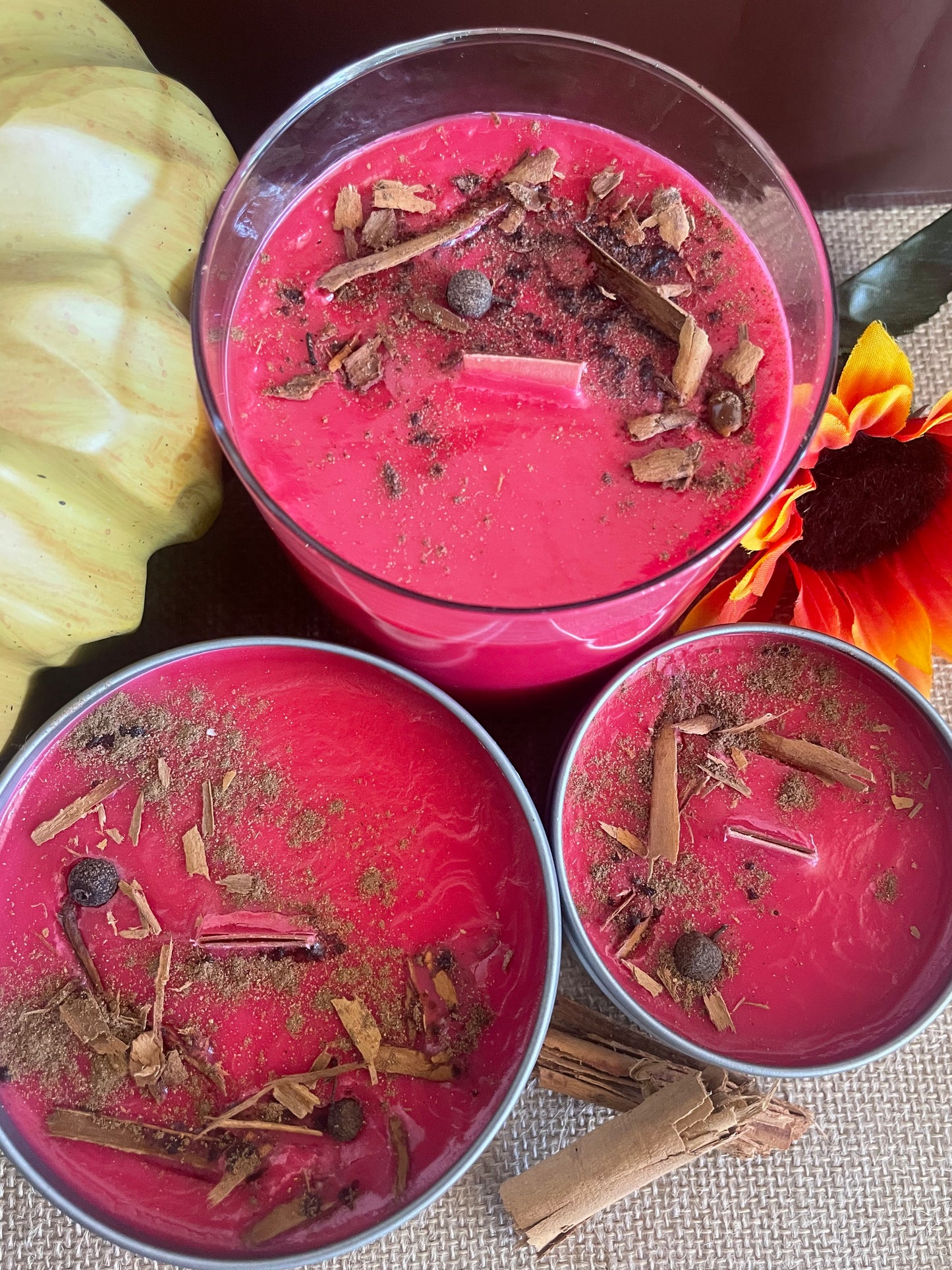 Three red candles with decorative elements in containers on a creamy wax and textured surface.