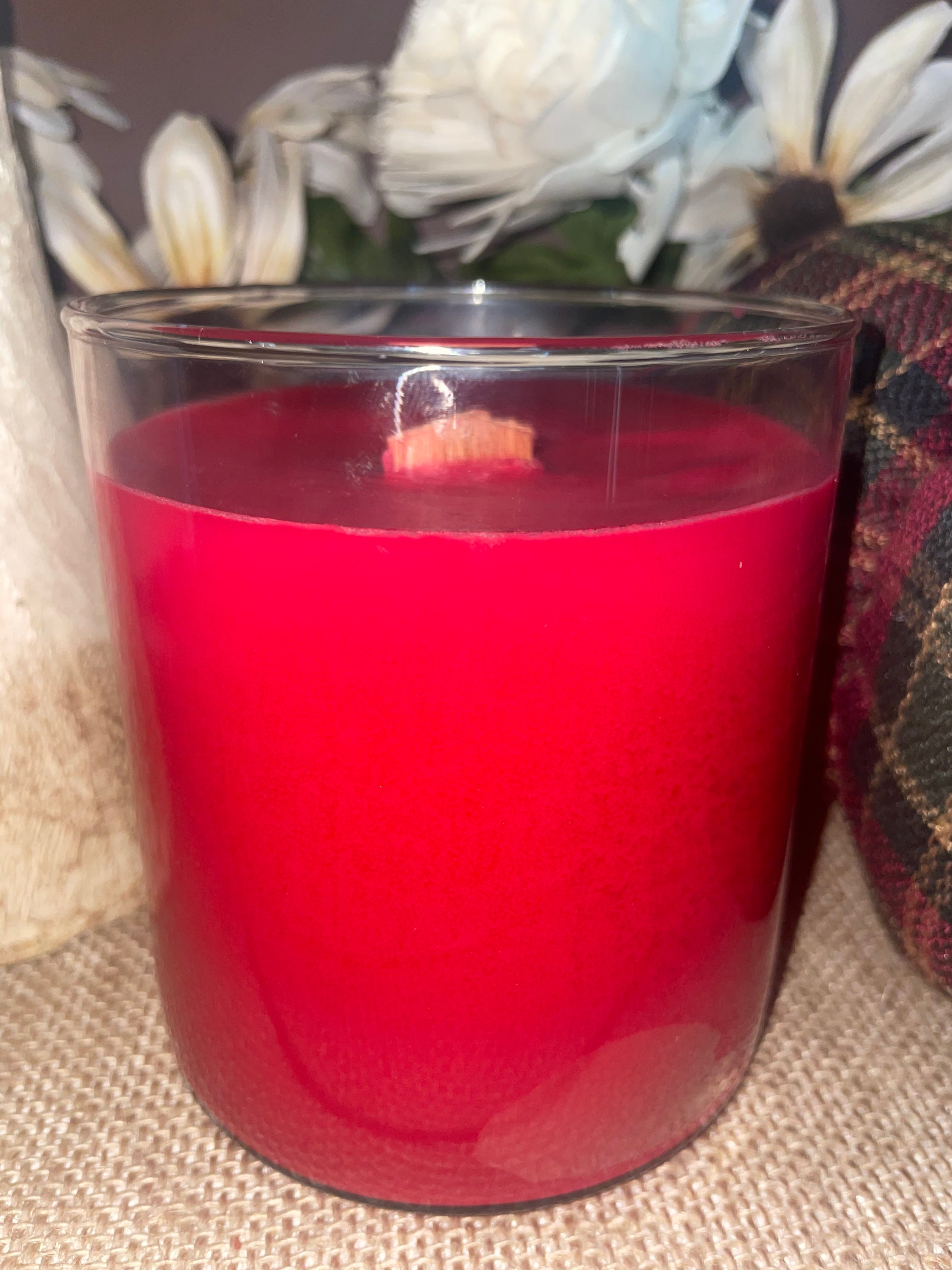 Red candle in a glass container on a textured surface with flowers in the background