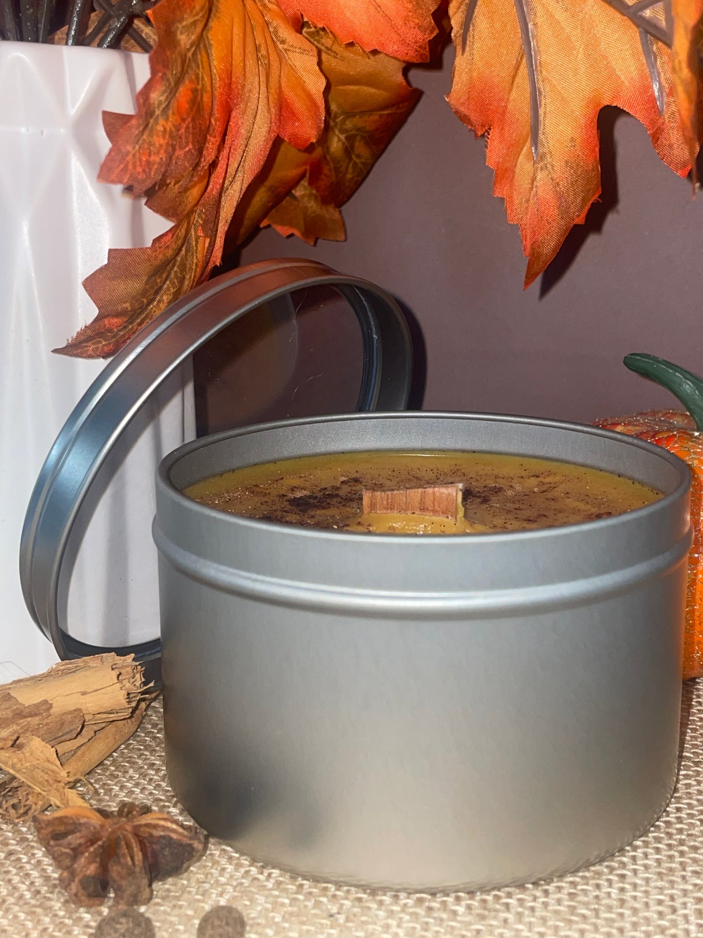 Candle in a tin with autumn leaves and cinnamon sticks on a textured surface