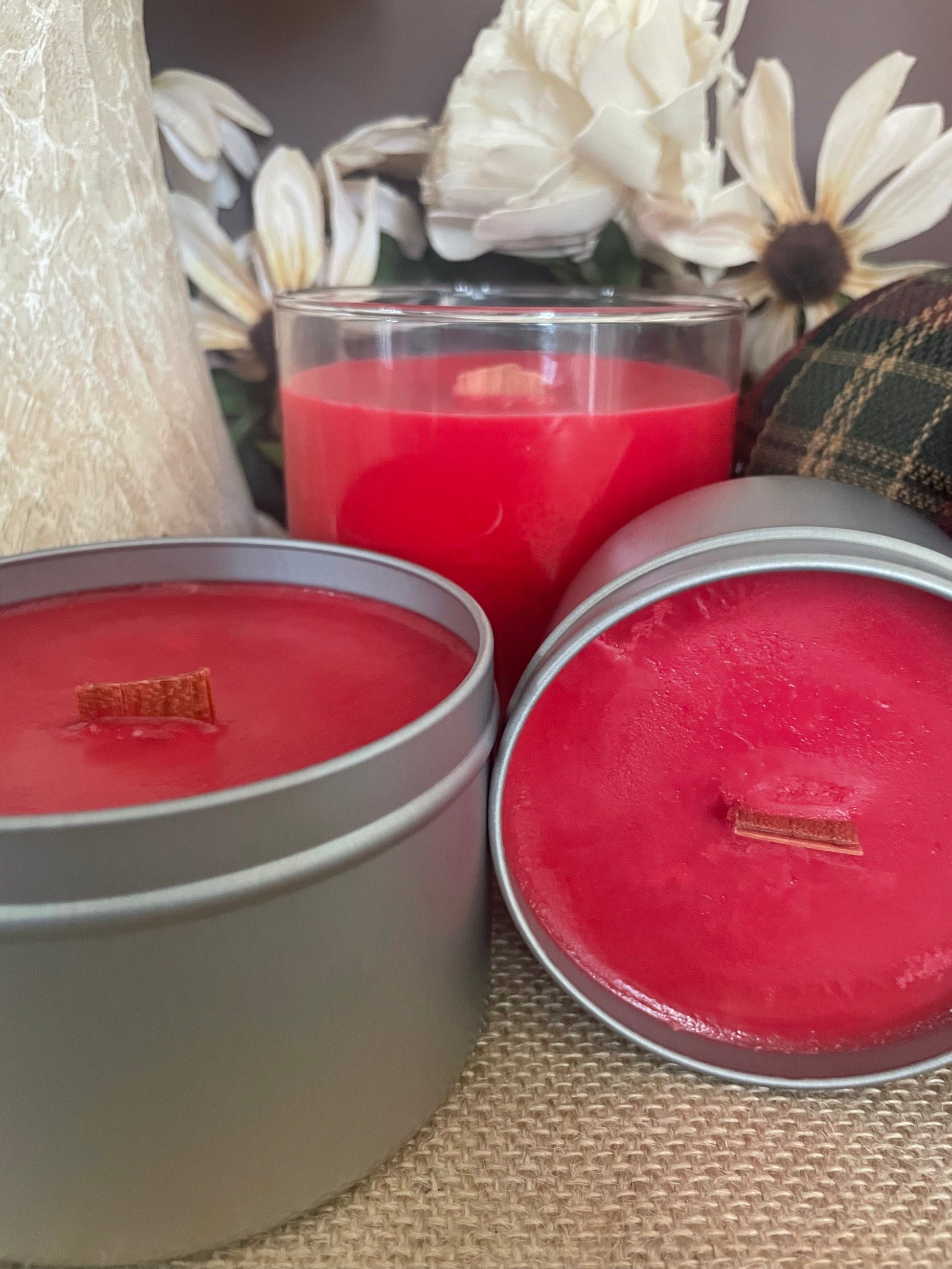 Three red candles in two in metal tins and one in a glass container with a decorative background