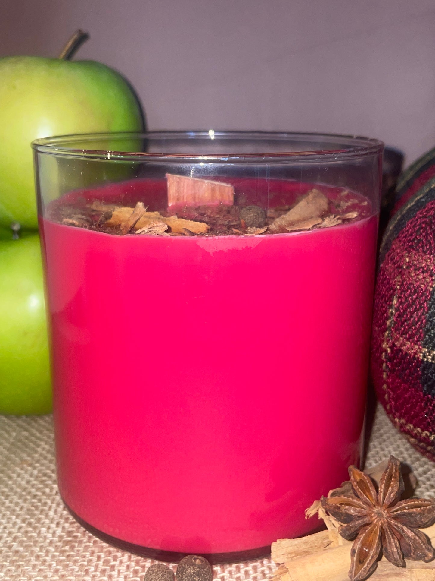 Red candle in a glass container with spices, decorated with an apple on a textured surface