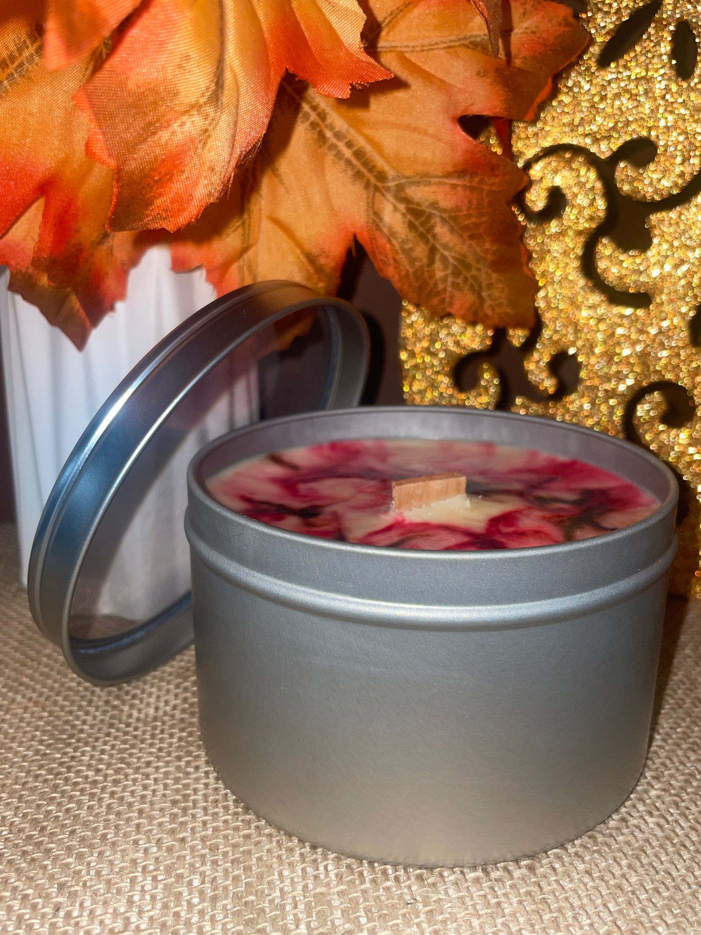 Candle in a tin with clear lid, unique fall color wax design on a creamy wax surface with leaves and gold background