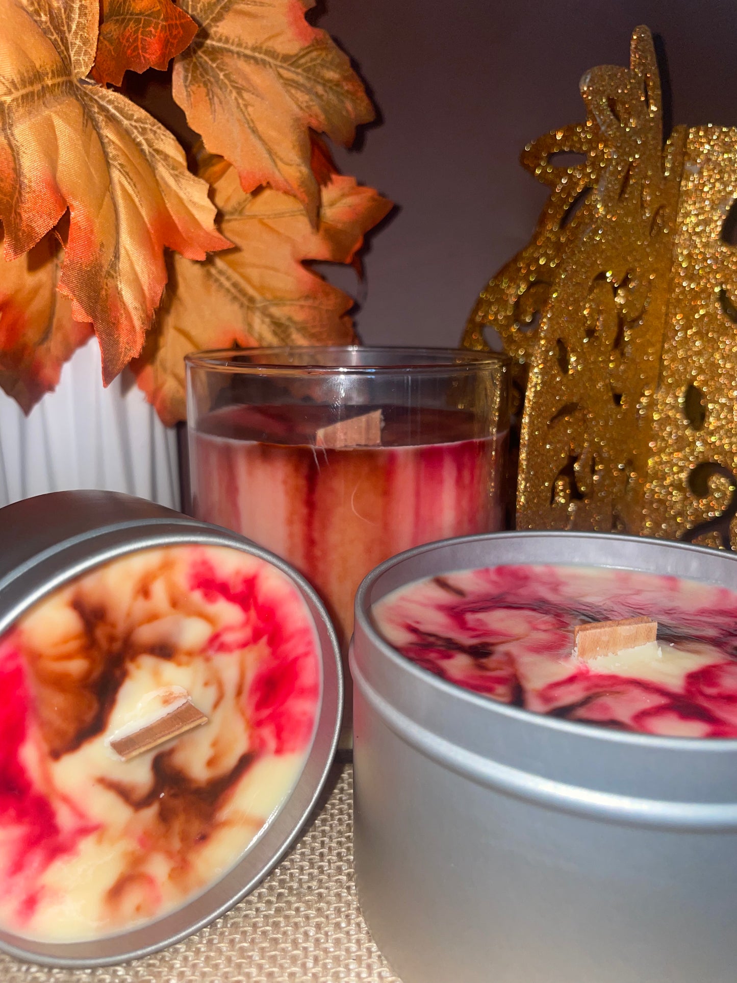 Unique candles featuring unique color designs, surrounded by autumn leaves and a gold ornament.