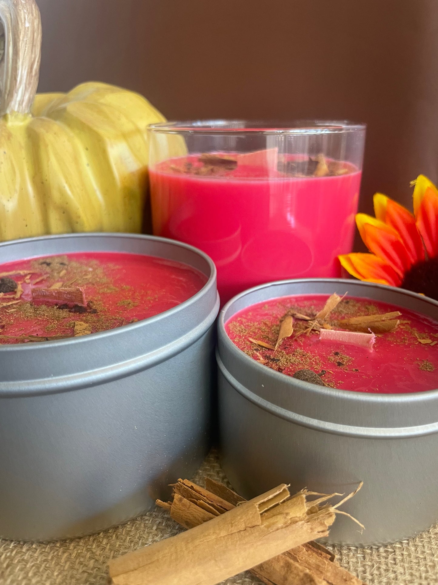 Red candles in containers with decorative elements on a brown background with a pumpkin and cinnamon sticks